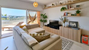 A modern living room with a sofa, TV, shelves with decorative items, and a view of the city.