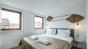 A bedroom with a bed, two windows, a wall-mounted fan, and a bedside table. - Nomad s Lux - 1bdr Charming Top Floor Porto (Porto)