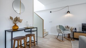 A modern living room with a black and white color scheme, a round mirror, a small table with stools, a rocking chair, and a staircase leading to an upper level. - Nomad s Lux - 1bdr Charming Top Floor Porto (Porto)