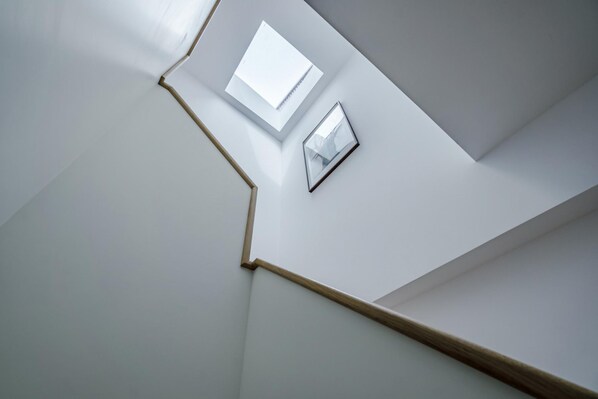 Un escalier moderne avec une rampe en bois et un mur blanc orné de deux tableaux encadrés.