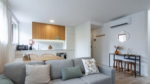 A modern living room with a grey sofa, a wooden dining table, and a kitchen area with white cabinets and a wooden countertop. - Nomad s Lux - 1bdr Charming Top Floor Porto (Porto)