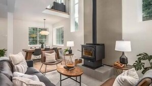 A modern living room with a fireplace, a dining area, and a staircase leading to an upper level. - Black Diamond Cabin | Private Hot Tub • Wood Fireplace • BBQ (Agassiz)
