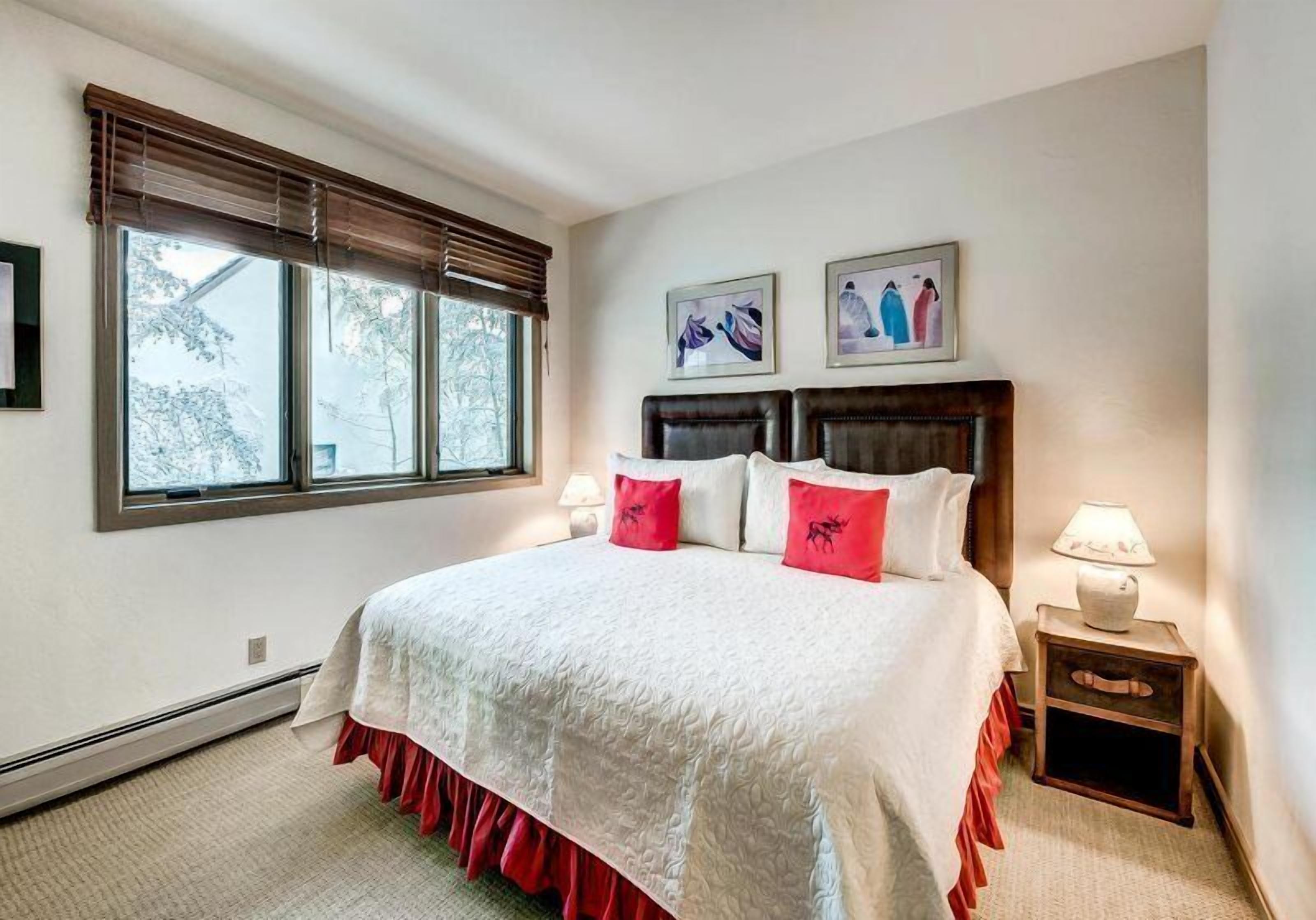 A bedroom with a large bed, two bedside tables, and a window with blinds.