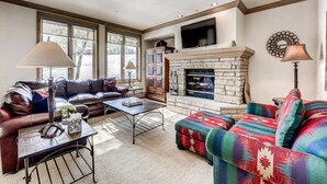 A living room with a stone fireplace, leather sofa, and a colorful patterned ottoman.