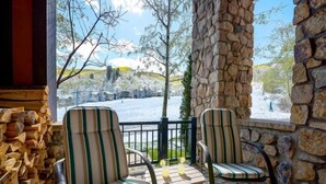 A patio with two striped chairs and a table, overlooking a snowy landscape with trees and a clear sky.