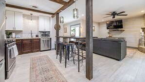 Una cocina moderna con vigas de madera, un comedor con taburetes de bar y un sofá gris en una sala de estar.