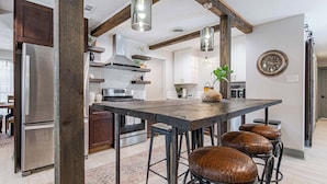 Una cocina moderna con una isla central, taburetes de bar, electrodomésticos de acero inoxidable e iluminación colgante.