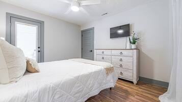 Une chambre à coucher avec un lit, une commode, un ventilateur de plafond et un téléviseur fixé au mur.