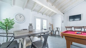 Una habitación con mesa de billar, sillas, un reloj y televisión.