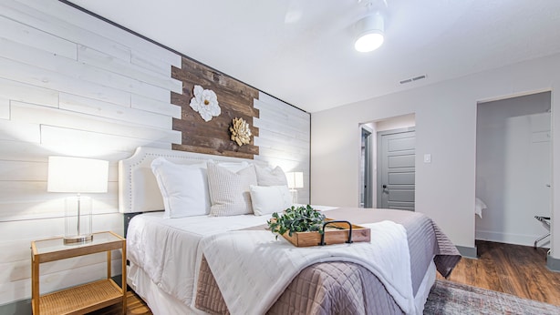 Un dormitorio moderno con cabecera de madera, una mesita de noche con lámpara y un adorno en la pared.