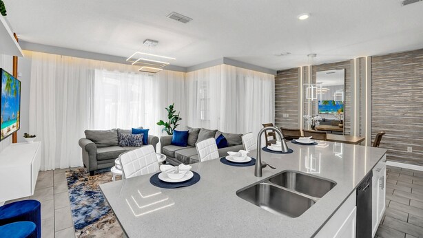 A modern kitchen with a central island, stainless steel sink, and a dining area with a white table and chairs. - Dream Disney Storey Lake House / private pool and 2 themed rooms 
 (Kissimmee)