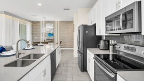 A modern kitchen with stainless steel appliances, a double sink, and a large island with seating. - Dream Disney Storey Lake House / private pool and 2 themed rooms 
 (Kissimmee)