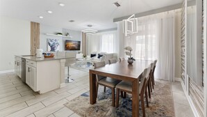 A modern kitchen with a central island, a dining area with a wooden table and chairs, and a living room with a sofa and a TV. - Dream Disney Storey Lake House / private pool and 2 themed rooms 
 (Kissimmee)
