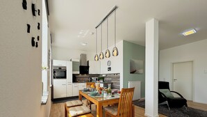A modern kitchen with white cabinets, a dining table with chairs, and pendant lights.