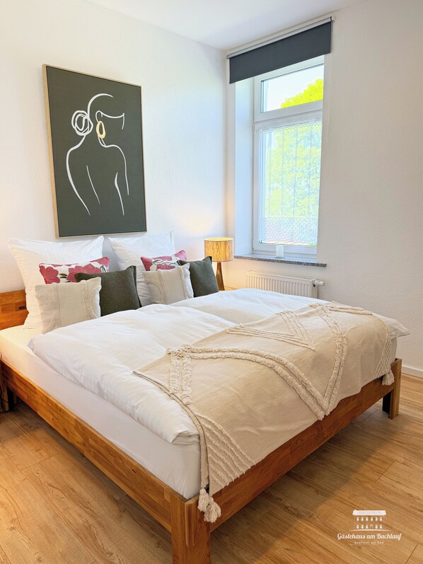 Un dormitorio con una cama de madera, ropa de cama blanca y un cuadro abstracto negro en la pared.