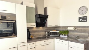 A modern kitchen with white cabinets, a built-in oven, a coffee maker, a microwave, and a clock on the wall.