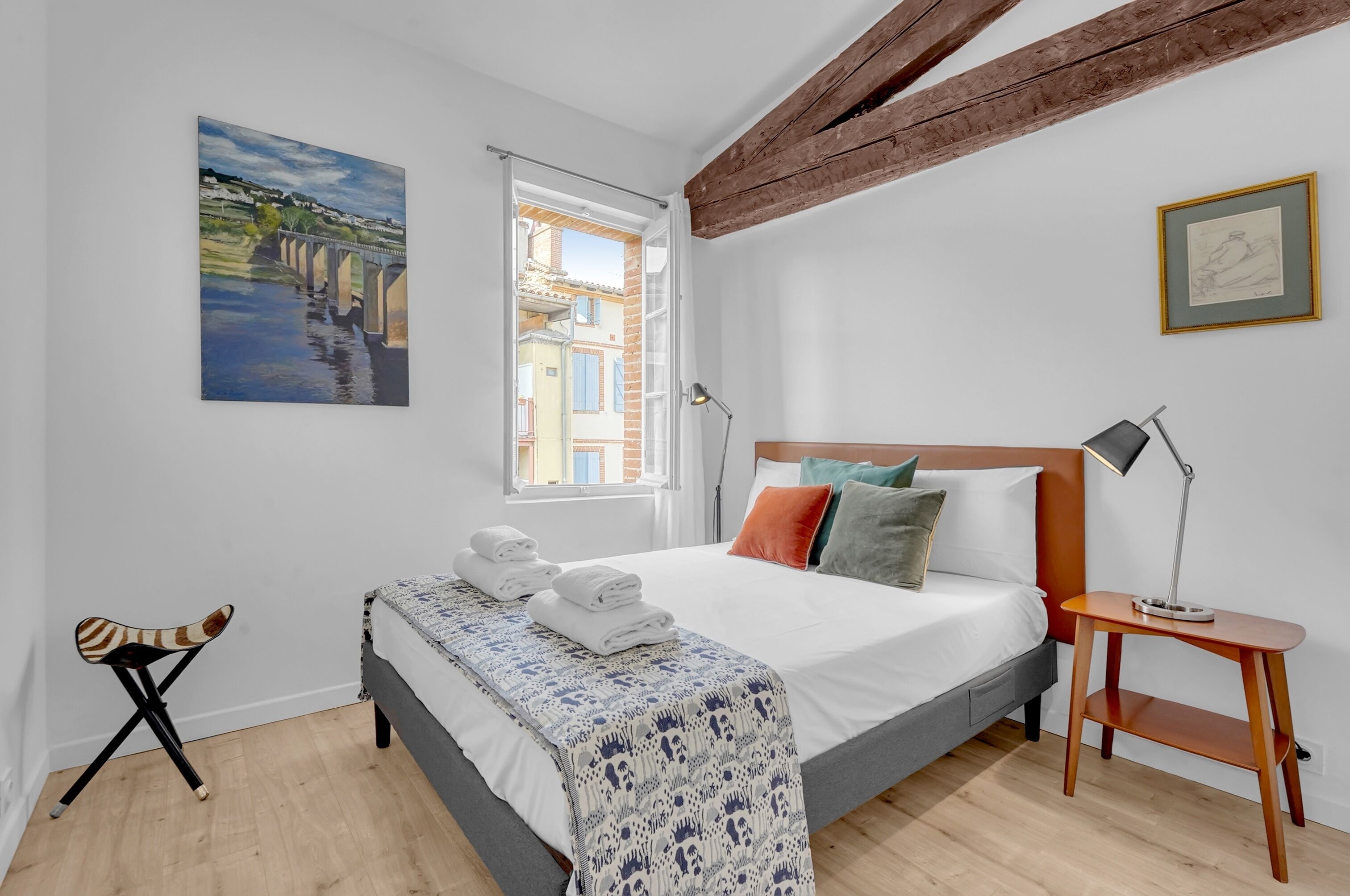 Une chambre à coucher avec un lit, une fenêtre, un tableau et une petite table.