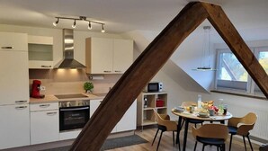 A modern kitchen with white cabinets, a stainless steel range hood, and a dining area with a round table and chairs. - Gästehaus am Bachlauf - Losheim am See 
Wohnung 6 – Weitblick (Losheim am See)