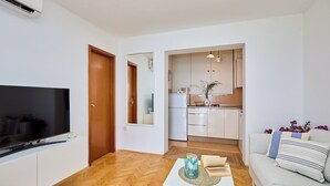 Un salon moderne avec un téléviseur à écran plat, un canapé blanc et une table basse agrémentée de livres et d’un objet décoratif.