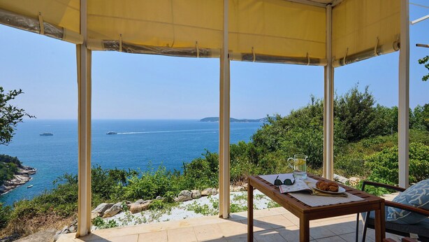 Un espace extérieur abrité, aménagé avec une table, des chaises et offrant une vue sur la mer.