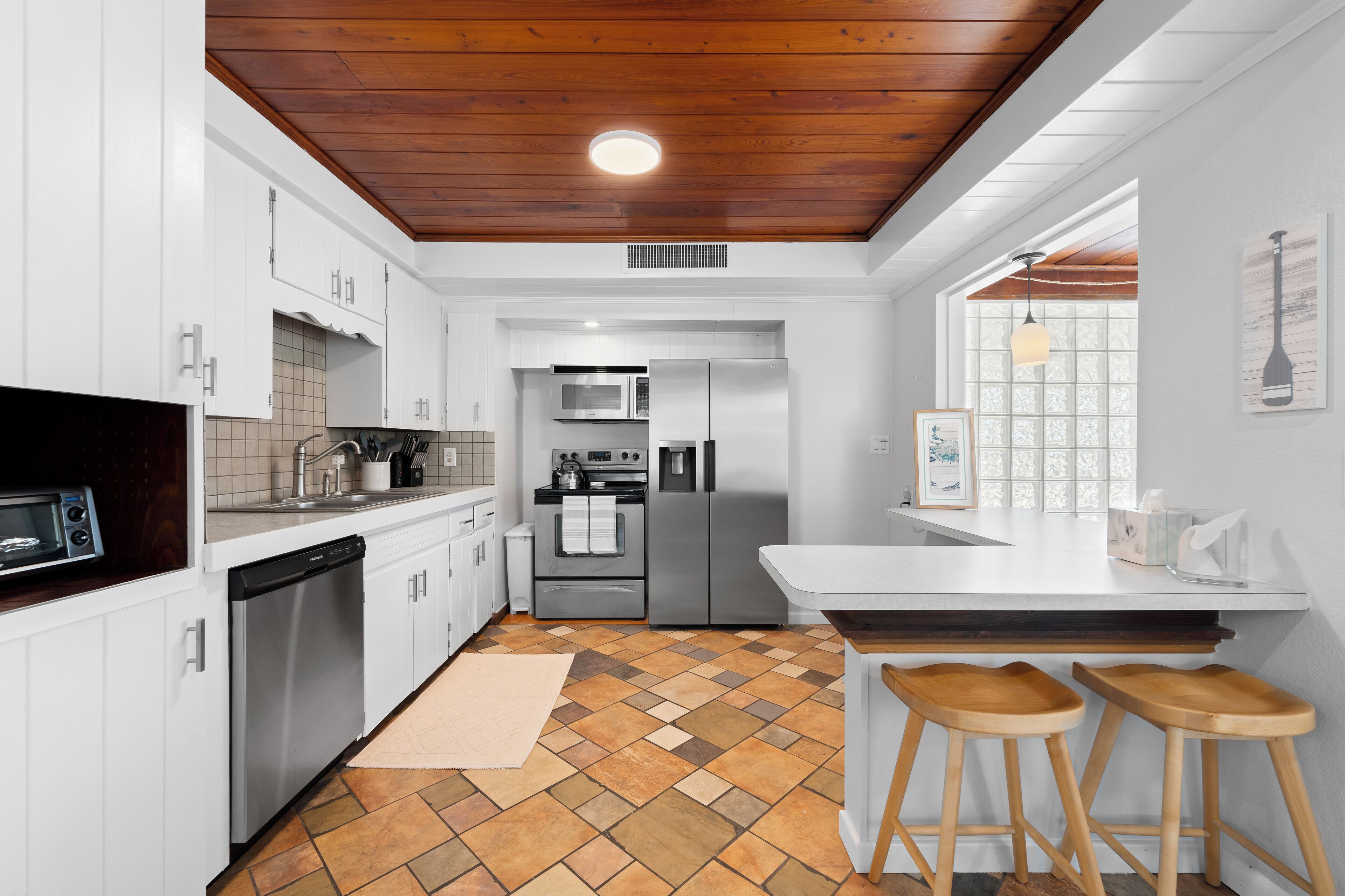 A modern kitchen with white cabinets, stainless steel appliances, a wooden ceiling, and a checkered floor.