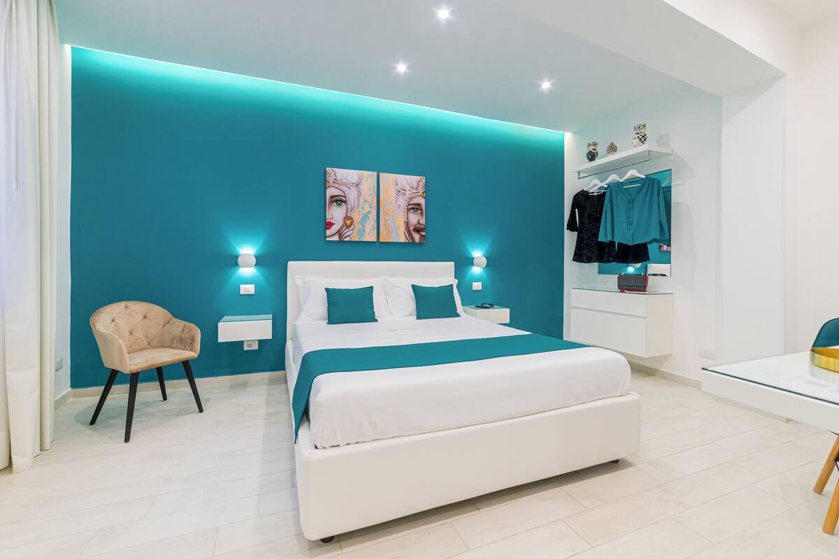 A modern bedroom with a large bed, a chair, a bedside table, and a wardrobe.