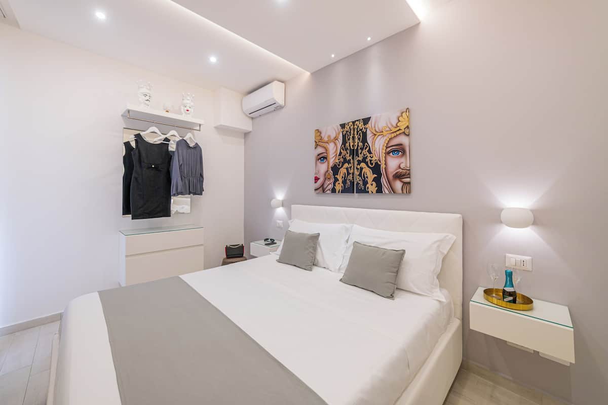 A modern bedroom with a large bed, a bedside table with a lamp, a wall-mounted air conditioner, and a clothing rack.