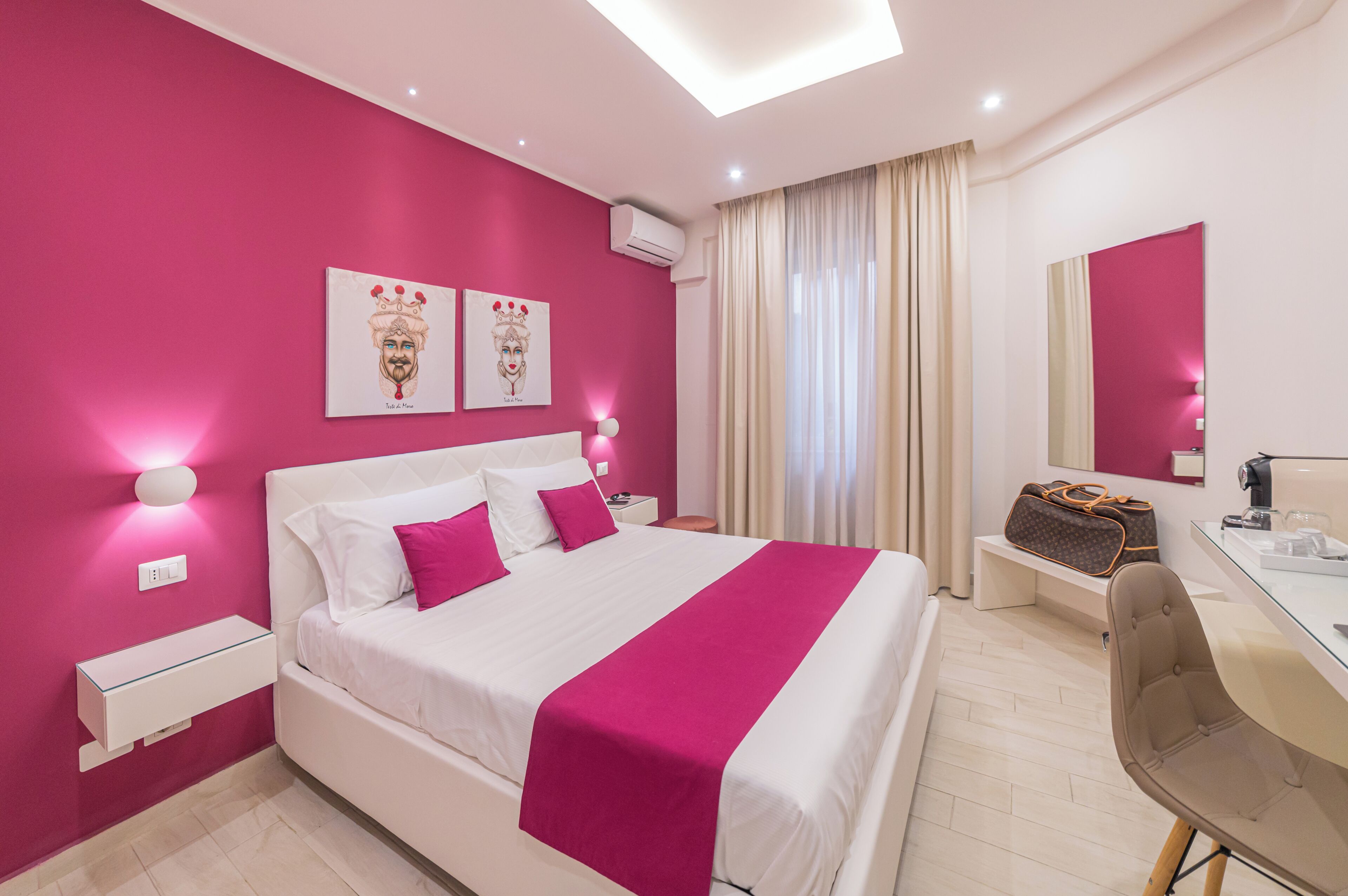 Habitación de hotel moderna con una cama grande, un escritorio y una silla. Hay un espejo en la pared, una maleta sobre el escritorio y una ventana con cortinas.
