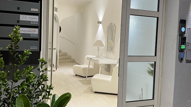 Een moderne hotelkamer met een glazen deur, een witte bank, een klein tafeltje en een lamp. Er is een trap die naar een ander niveau leidt.
