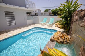 A swimming pool with two lounge chairs, a rock feature, and a plant. - R&V Combate Beach House 1 with Pool (Cabo Rojo)
