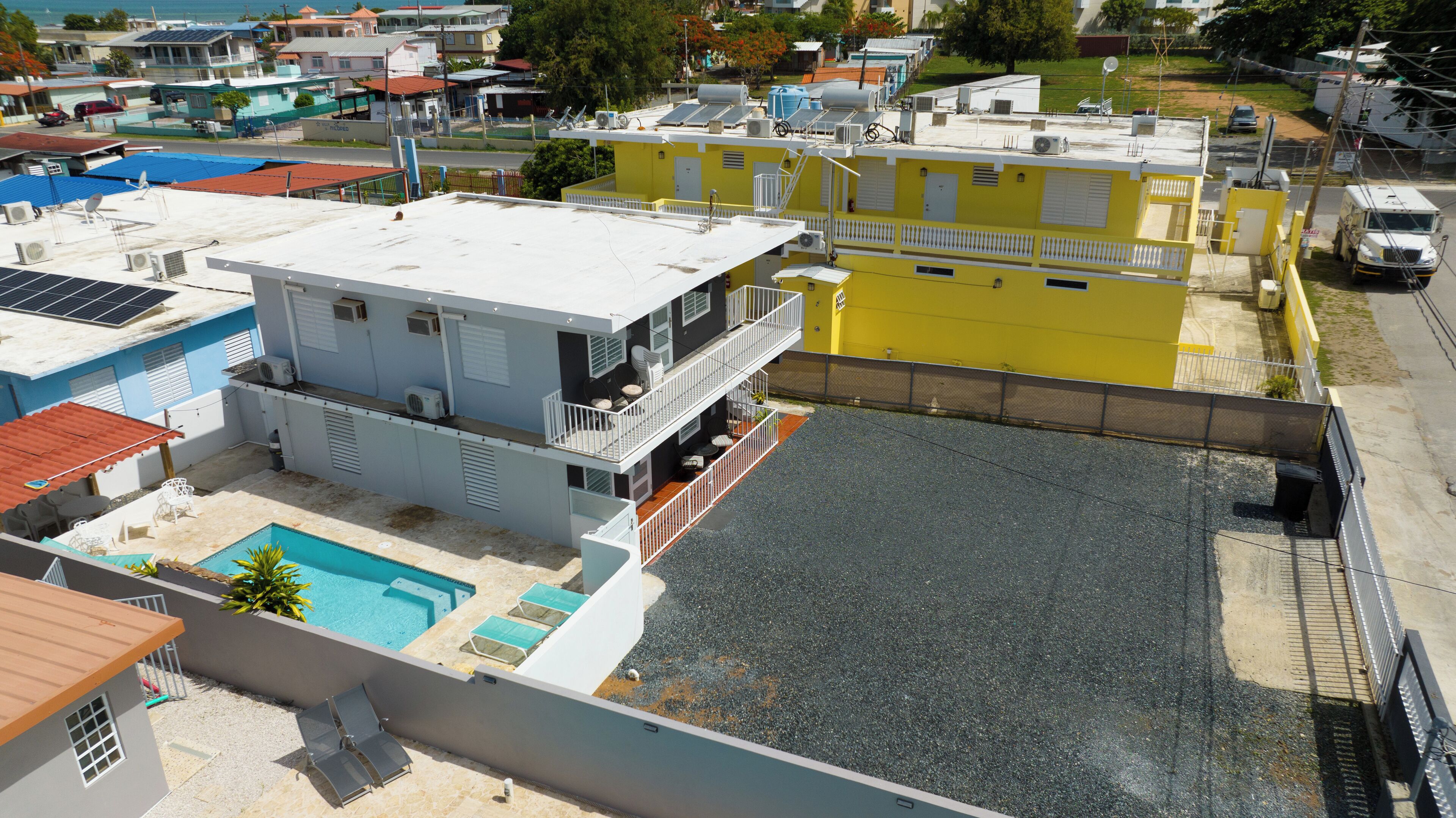 A multi-story building with a rooftop pool, a covered outdoor area, and a yellow building adjacent to it.