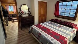 Un dormitorio con cama, cómoda, espejo, ventana con cortinas y puerta que da a otra habitación.