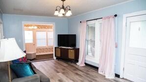 A living room with a grey sofa, a TV on a wooden cabinet, and a chandelier.