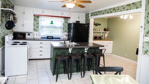 A kitchen with white cabinets, a black refrigerator, a stove, and a bar area with stools.