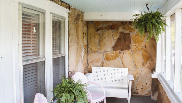 A covered porch with two rocking chairs, a table, and a hanging plant.