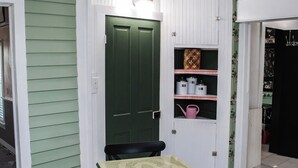 A dining area with a green table and chairs, a white door, and a shelf with kitchen items.