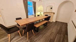 Un comedor con una mesa de madera y sillas negras, un banco, una chimenea y una ventana con cortinas.