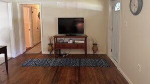 Un salon avec un téléviseur posé sur un meuble en bois, un tapis à motifs et une horloge au mur.