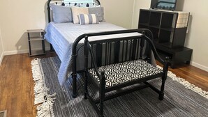 Une chambre à coucher avec un lit, un berceau en métal noir, un meuble pour la télévision et des tableaux encadrés accrochés au mur.