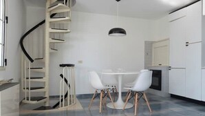 Eine moderne Küche mit einer weißen Wendeltreppe, einem runden Esstisch mit weißen Stühlen und einer Pendelleuchte.