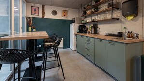 A kitchen with a wooden table and bar stools, a microwave, and shelves with glassware and plants. - Ambrosia Hüsli (Rheinfelden)