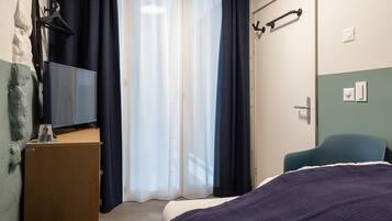 A hotel room with a bed, a desk with a lamp, a chair, and a window with curtains.
