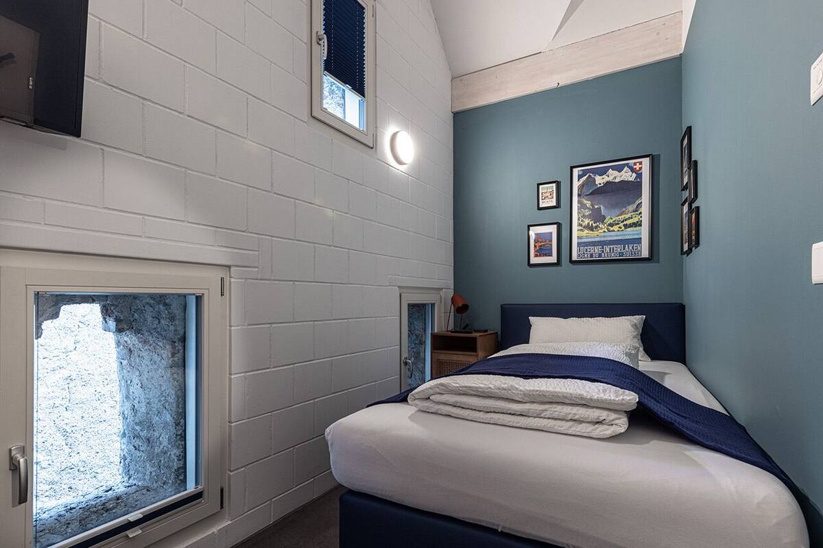A bedroom with a bed, a window, and a wall-mounted shelf.
