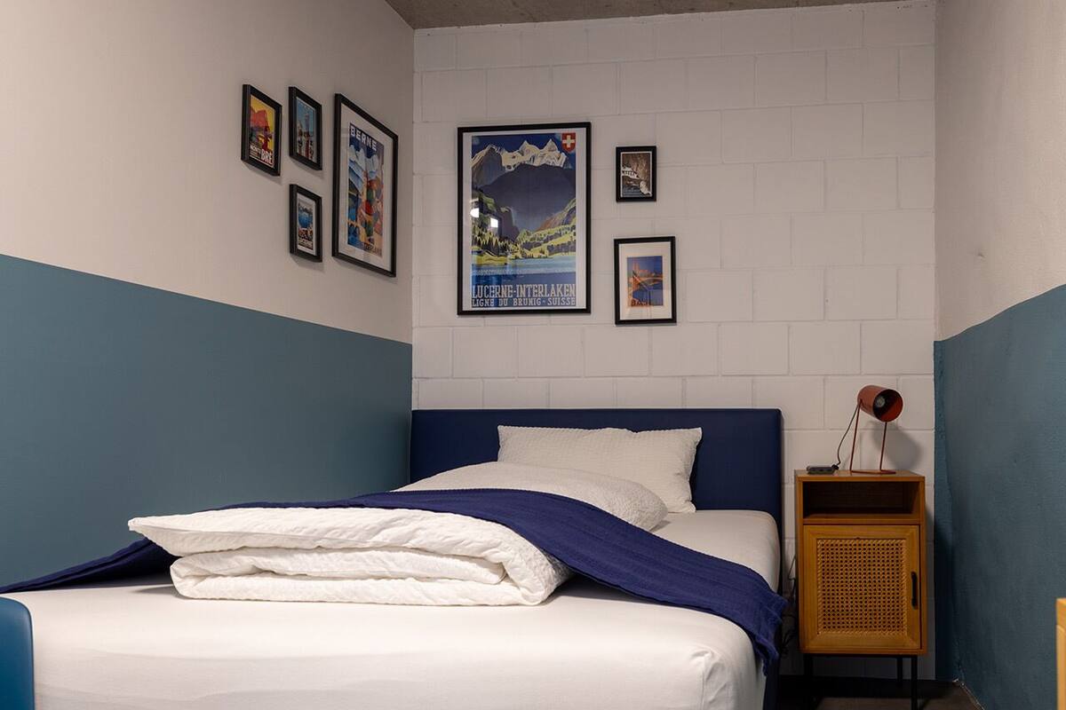 A bedroom with a bed, a nightstand, and a wall with framed pictures.