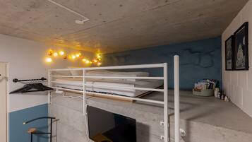 A bunk bed with a white frame, a shelf above, and a concrete wall with a blue accent.