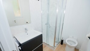 Un baño moderno con cabina de ducha de vidrio, lavamanos blanco y retrete.