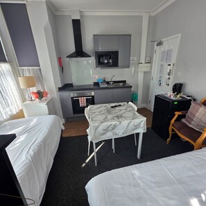 A compact hotel room with a bed, a small table, a kitchenette, and a seating area.