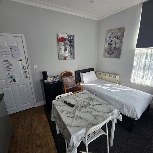 A hotel room with a bed, a small table, a chair, a desk, and a radiator.