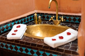 Une salle de bain avec un lavabo doré, des carreaux bleus et noirs à motifs, et deux serviettes blanches ornées de cœurs rouges.