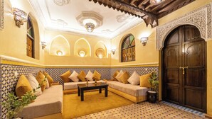A traditional Moroccan interior with a sofa set, patterned walls, and a large wooden door.